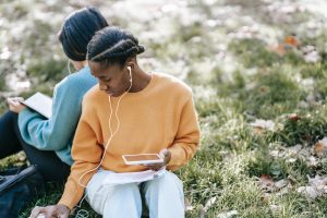 two young people sitting on grass wearing earbuds