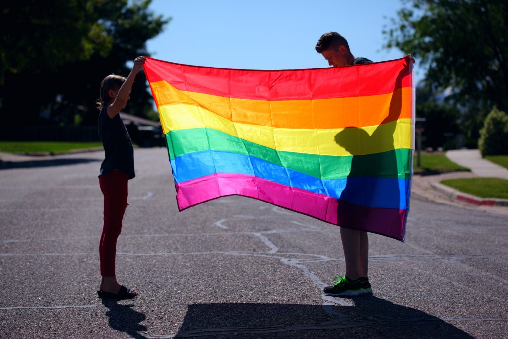 a child and parent silhouetted behind a rainbow flag